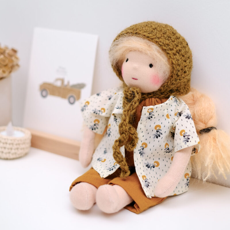 Poupée Waldorf artisanale rembourrée de laine vierge, vêtue d’une blouse fleurie et d’un pantalon.